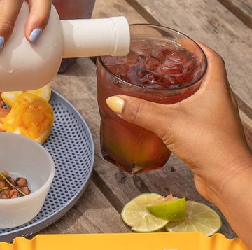 hand pouring haus into glass of ice at picnic table