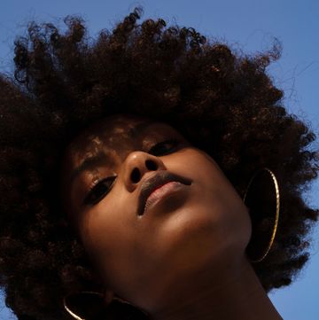 low angle shot beautiful black woman with afro wearing yellow dress against blue sky