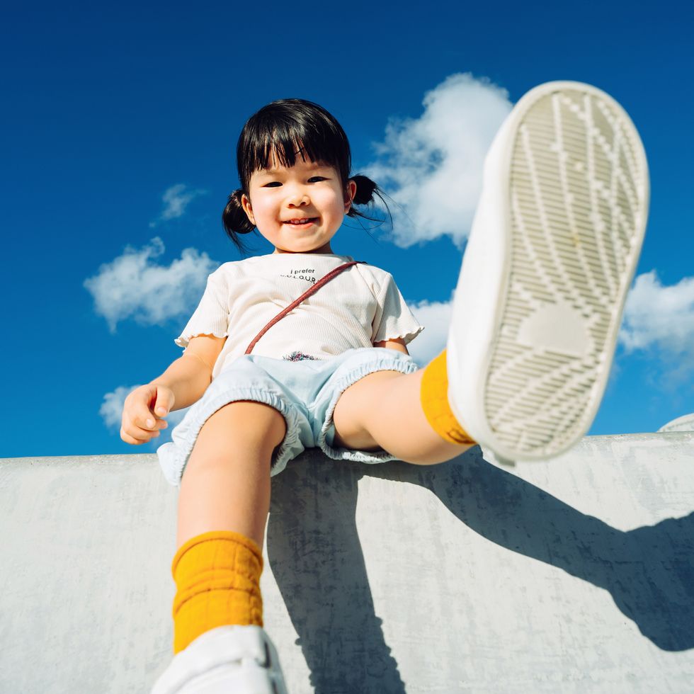 low angle view of cute little asian girl smiling joyfully and having fun in outdoor park against beautiful blue sky on a lovely sunny day