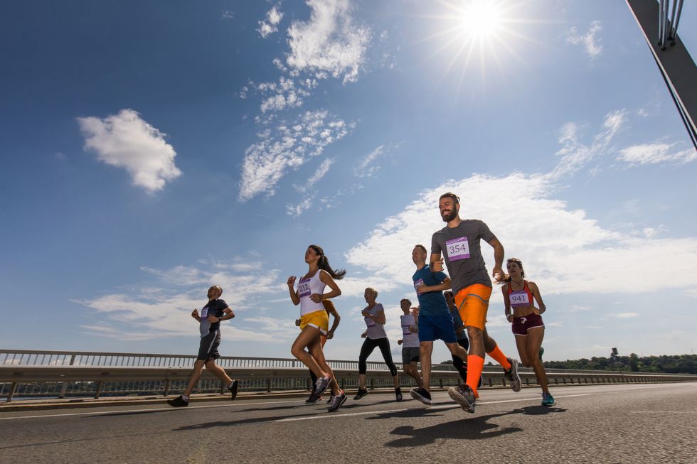 Low angle view of large group of happy athletic people running a marathon race on the road.