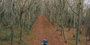 low angled drone view of a runner on a treelined trail