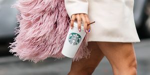 a stylish woman wears a white long jacket and holds a starbucks coffee cup