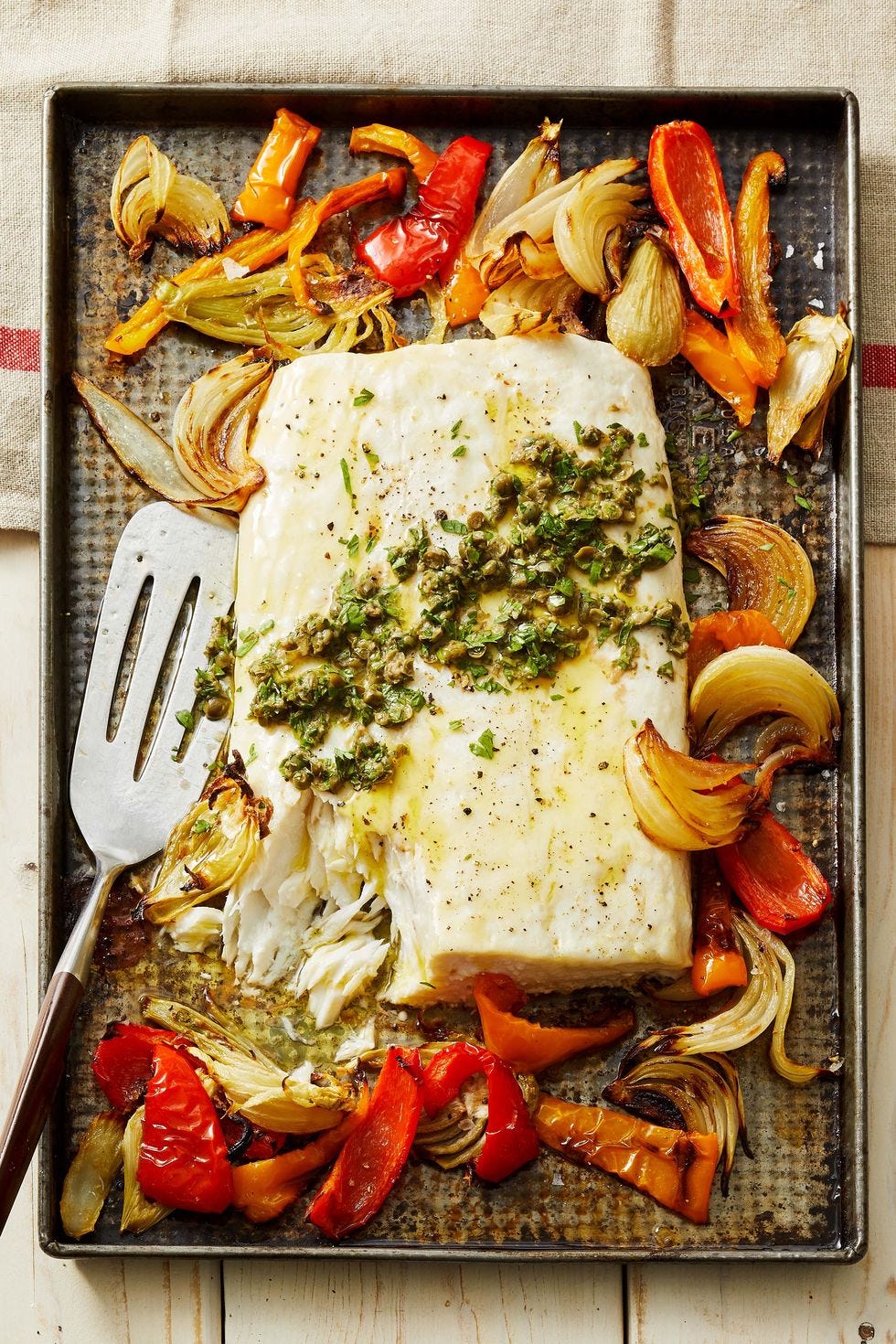 a sheet pan with fish and roasted peppers and onions and a spatula