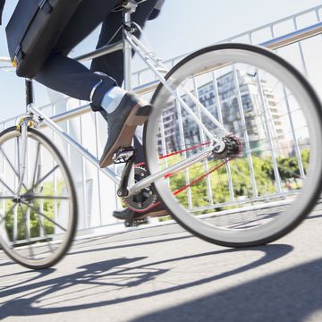 Low section businessman in suit riding bicycle on sunny urban sidewalk