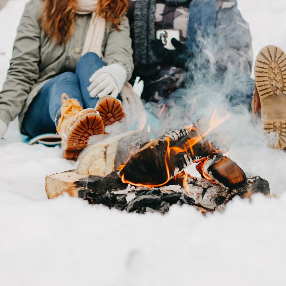 low section of couple siting by bonfire on snow covered land