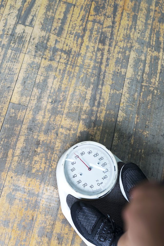 low section of man checking weight on bathroom scale in gym