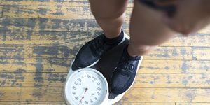 low section of man checking weight on scale in gym