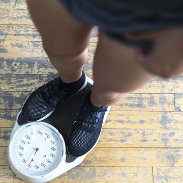 low section of man checking weight on scale in gym