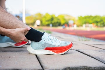 low section of man holding aching ankle while kneeling outdoors