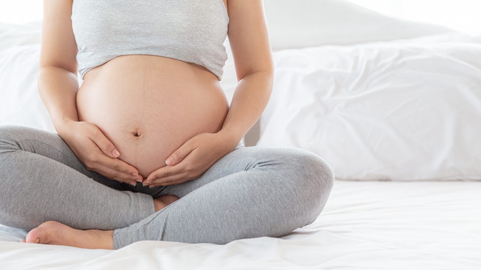 una chica se acaricia la barriga embarazada con un conjunto de deporte gris