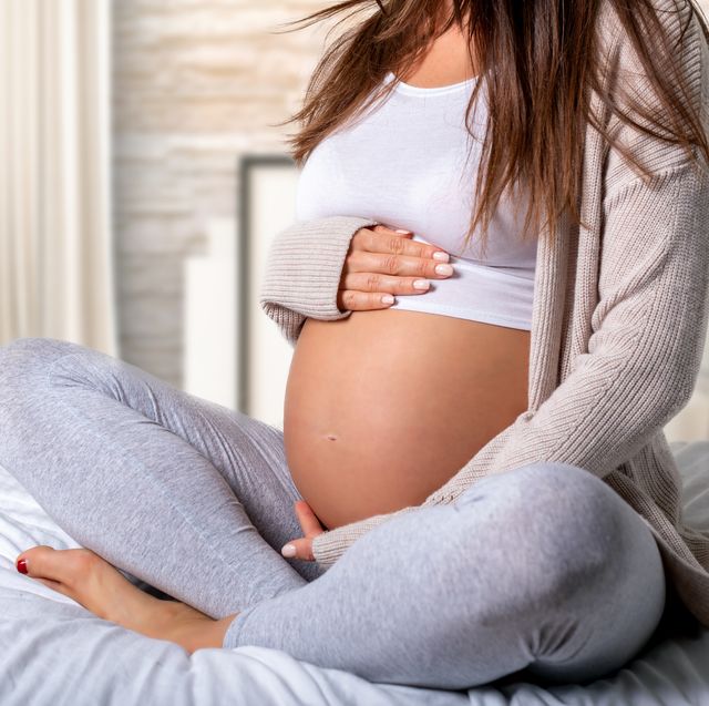 Low Section Of Pregnant Woman Touching Belly While Sitting On Bed