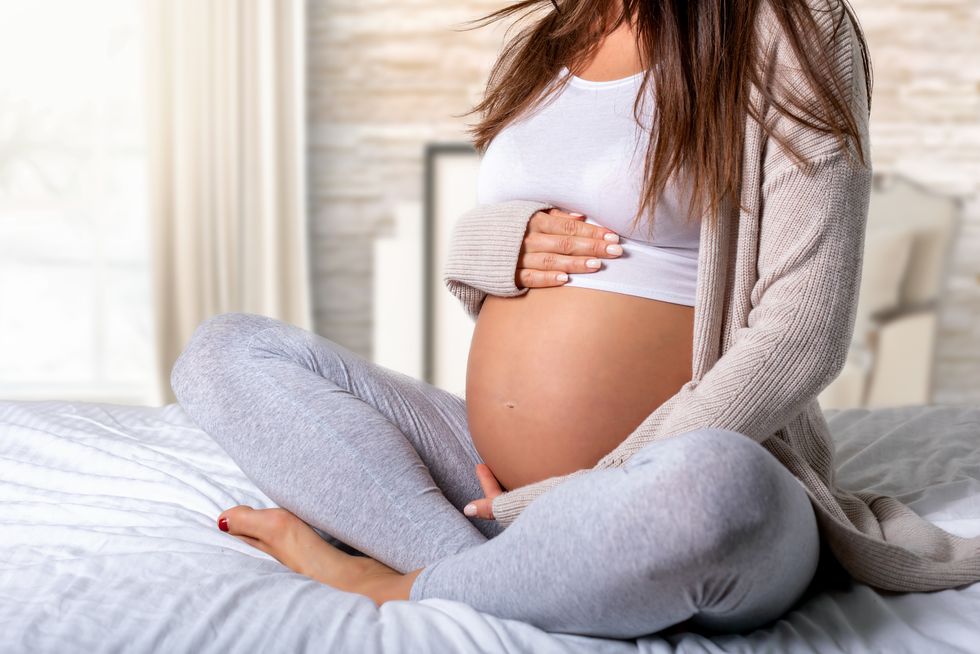 low section of pregnant woman touching belly while sitting on bed