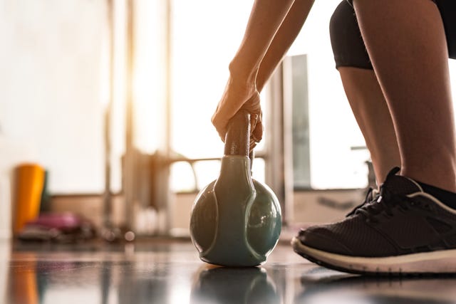Low Section Of Woman Lifting Kettlebell At Gym