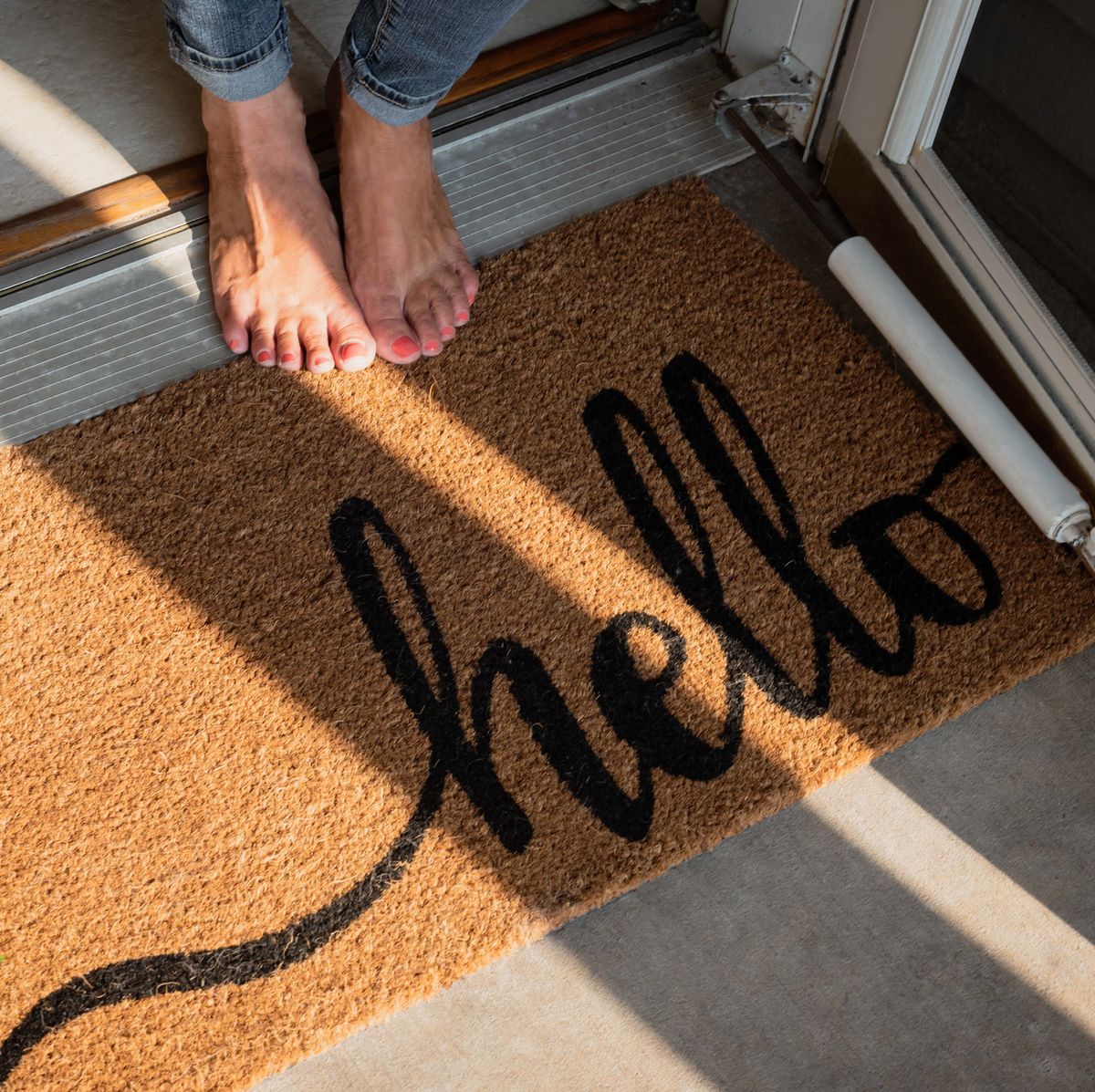 Low Section Of Woman Standing By Doormat With Hello Text