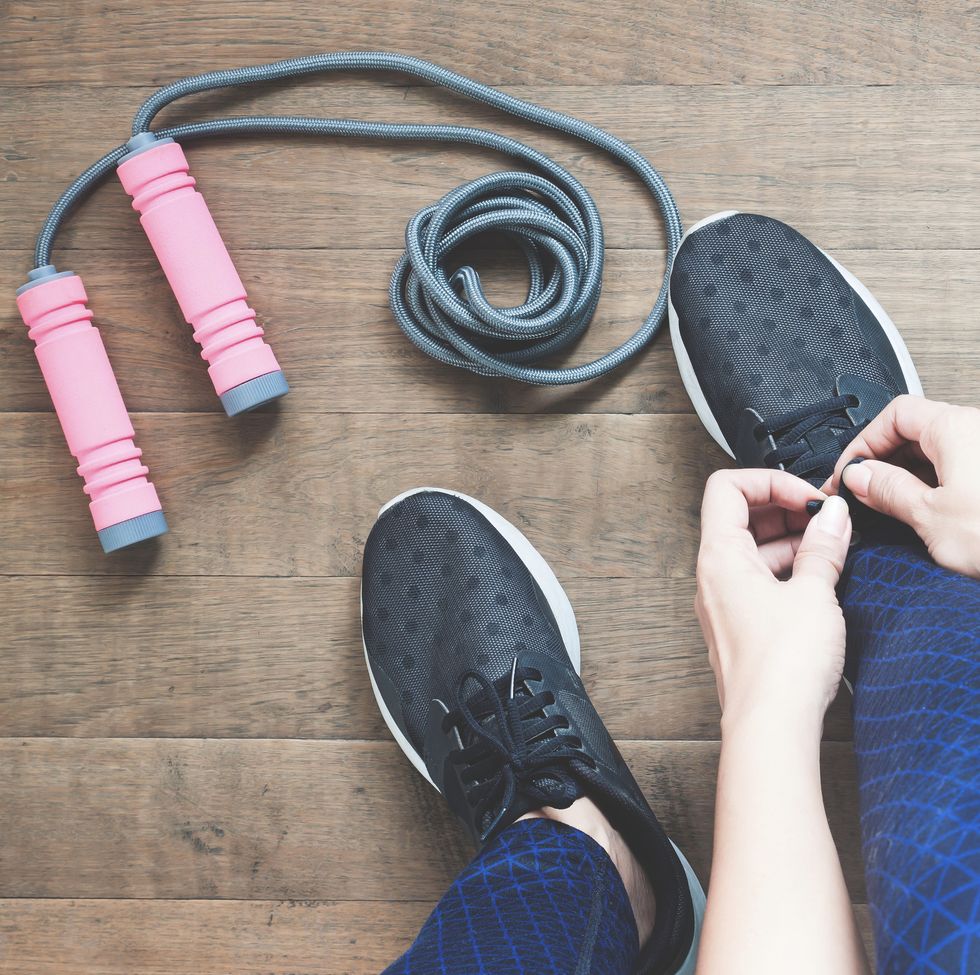 low section of woman tying shoelace by skipping rope on hardwood floor