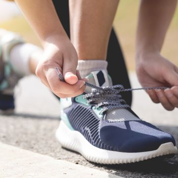 Low Section Of Woman Tying Shoelace On Road