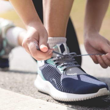 Low Section Of Woman Tying Shoelace On Road Low Section Of Woman Tying Shoelace On Road
