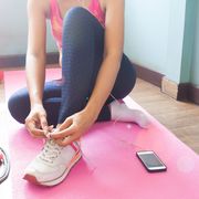 low section of woman tying shoelace while sitting on exercise mat at home
