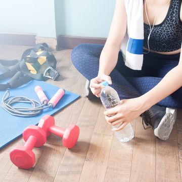 Low Section Of Woman With Water Bottle By Dumbbells On Hardwood Floor