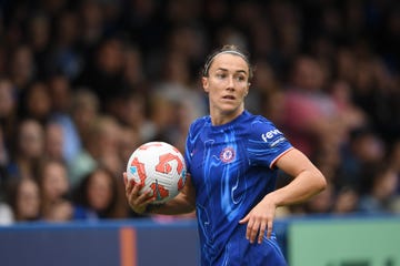 chelsea football player lucy bronze holds a football in her right hand as she stands on the pitch during a game