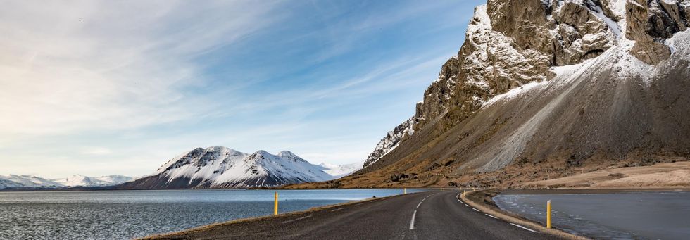 a road next to a body of water with mountains in the background
