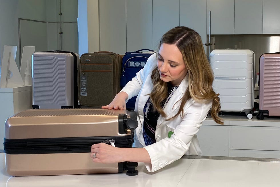 a woman unzipping a hardside suitcase on a table
