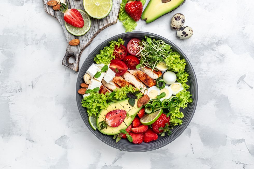 lunch bowl with chicken, avocado, feta cheese, quail eggs, strawberries, nuts and lettuce detox and healthy superfoods bowl concept top view