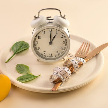 Healthy food diet concept. healthy food composition with cutlery, plate, measuring tape, yellow dumbbell, green vegetable salad leaves and alarm clock on pastel beige background dieting and keep fit close up copy space front view