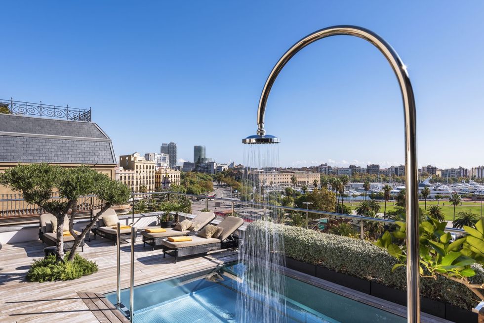 a pool framed by a large shower tap and buildings in the background