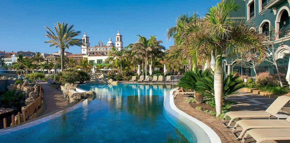 a pool with palm trees and lopesan villa del conde resort and thalasso in the background