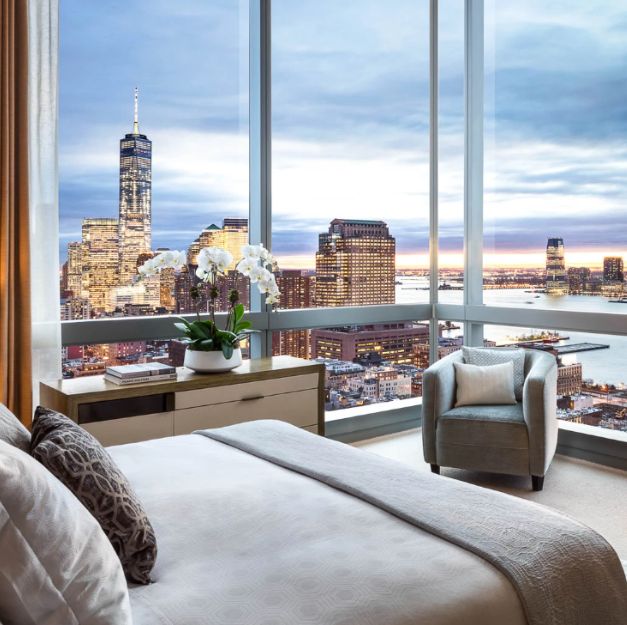 a room with a large corner window and a bed with a view of a city