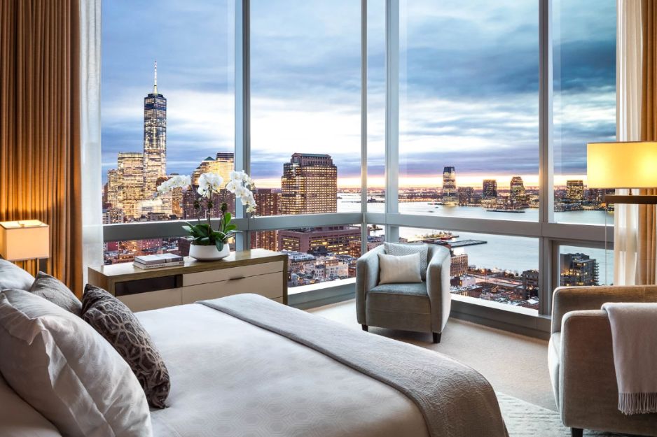 a room with a large corner window and a bed with a view of a city