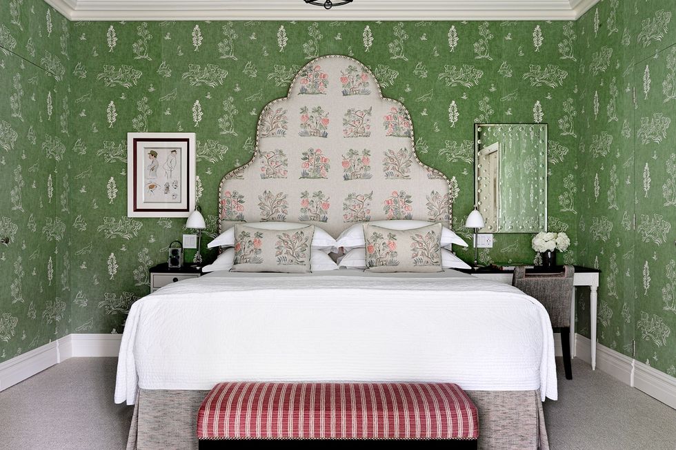 a big bed with floral headboard against a green wall