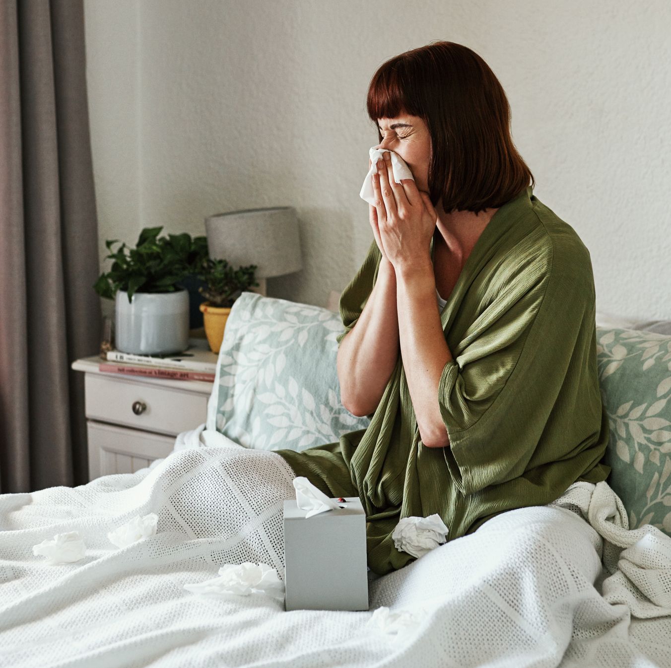 woman sneezing in bed with tissues