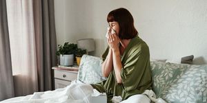 woman sneezing in bed with tissues