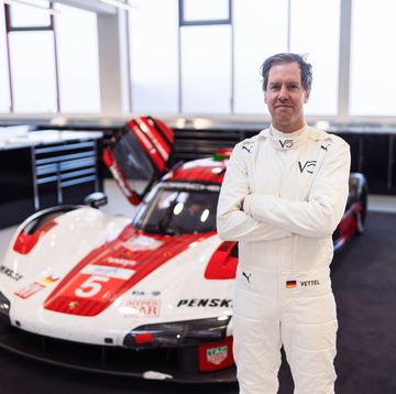 a man in a white suit standing next to a race car