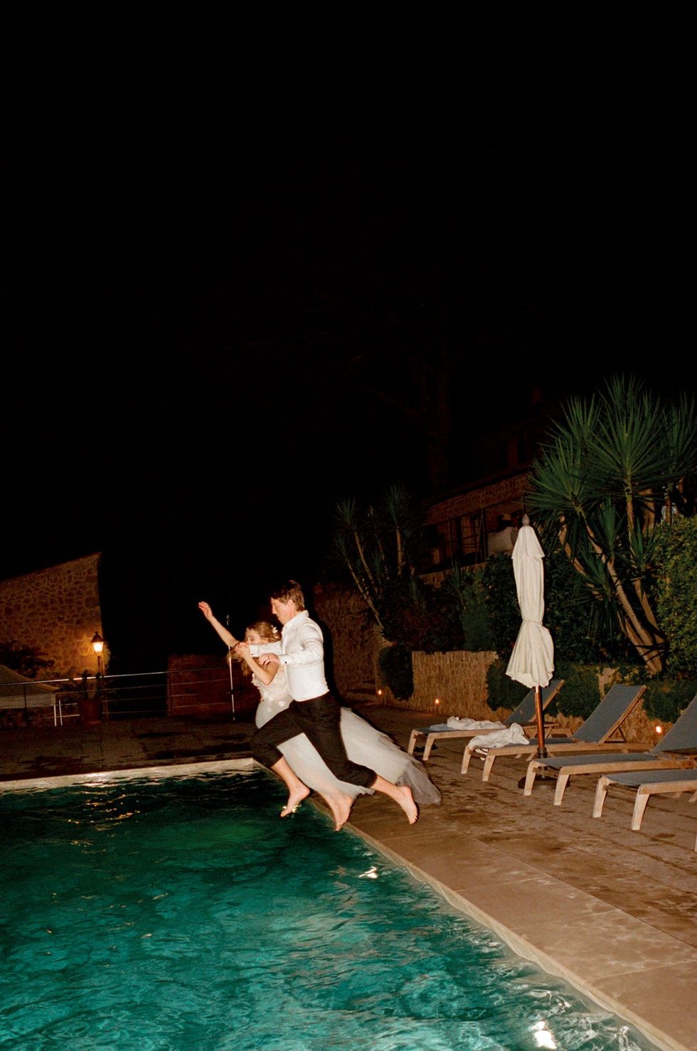 a man and woman dancing by a pool at night