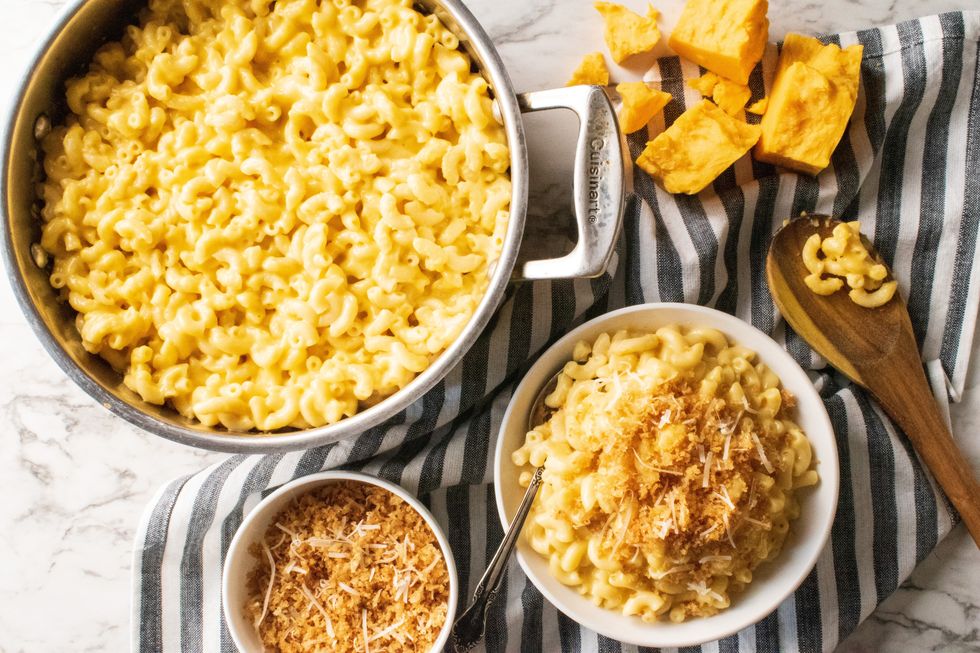 a pot of macaroni and cheese next to a bowl of macaroni and cheese on top a pinstriped towel