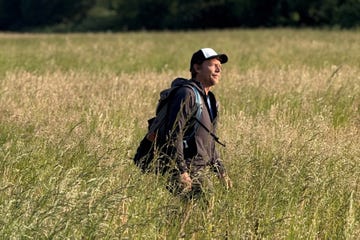 person walking through a tall grassy field with a backpack