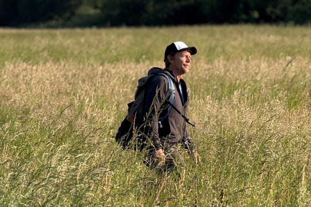 person walking through a tall grassy field with a backpack