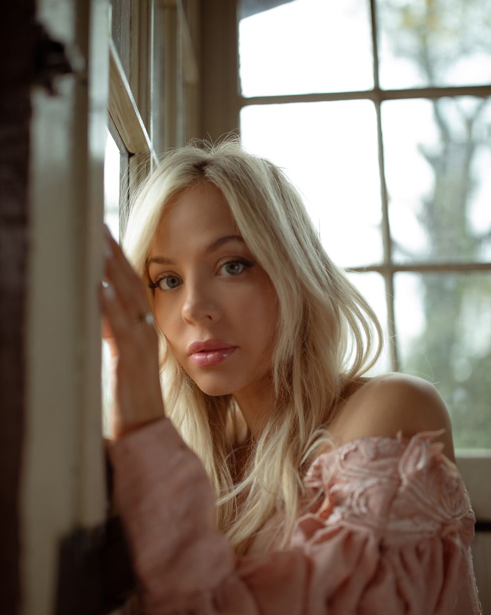 country singer songwriter mackenzie porter in pink off shoulder western style dress standing in farmhouse with natural light
