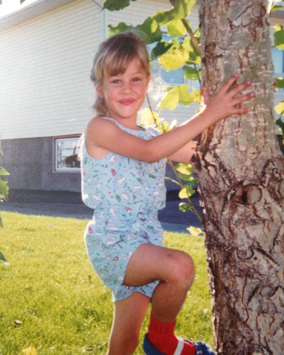mackenzie porter as a child posing next to a tree