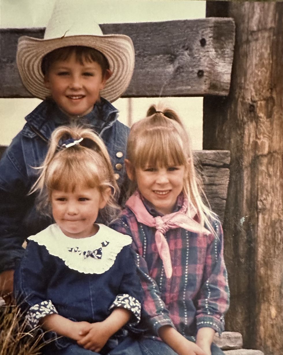 mackenzie porter with her brother and sister as children sitting in front of a rustic wood beam fence