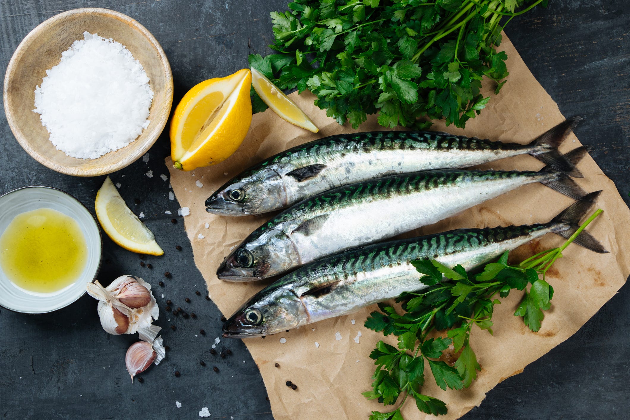 fresh mackerel fish on paper with lemon, salt, olive oil, garlic, parsley and pepper