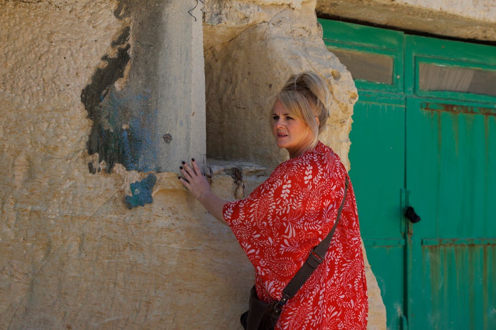 A person is resting their hand on a textured stone wall beside a closed green door