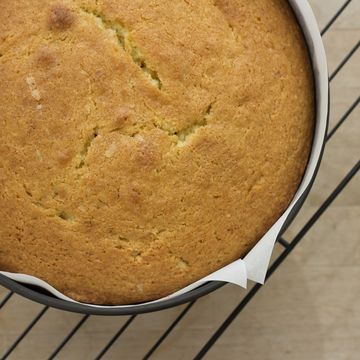 a round shaped madeira cake in a baking tin, parchment paper on a wire cooling rack