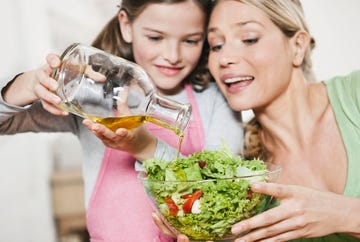 una mujer y su hija aliñan una ensalada con aceite de oliva