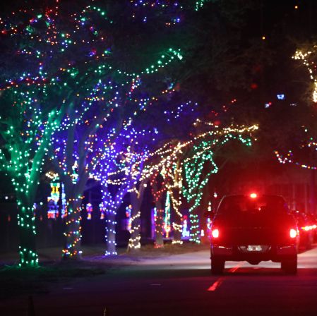 car riding down road with brightly colored christmas lights strung throughout the trees on both sides