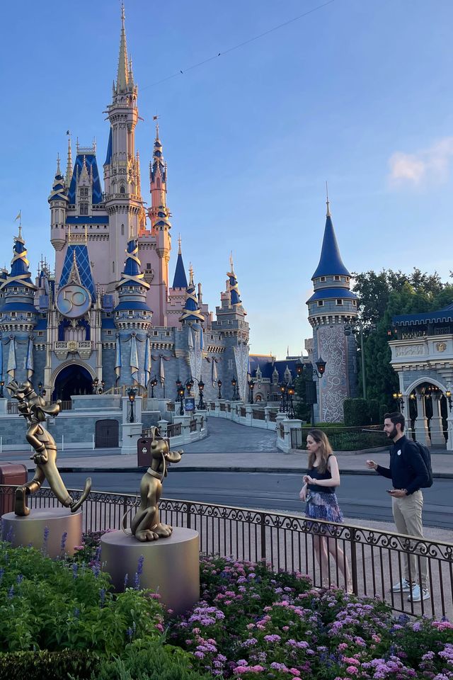good housekeeping's lexie sachs trying out disney's magicband plus with jc diaz in front of golden character statues at magic kingdom park
