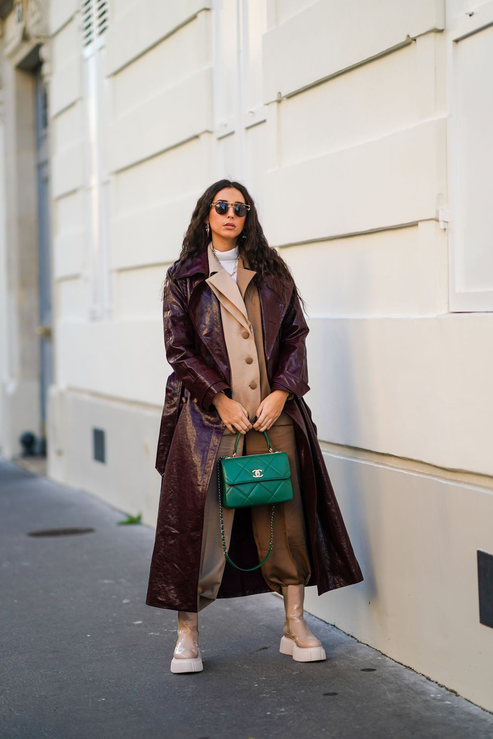 paris, france   december 15 gabriella berdugo wears  sunglasses, a white turtleneck pullover, earrings, a necklace, a bi color beige and brown oversized blazer jacket and suit pants from salisa nyc, beige nude biker platform shiny boots from agl, a leather vynil aubergine colored  purple trench coat from maison natan, a green quilted leather chanel bag, on december 15, 2020 in paris, france photo by edward berthelotgetty images